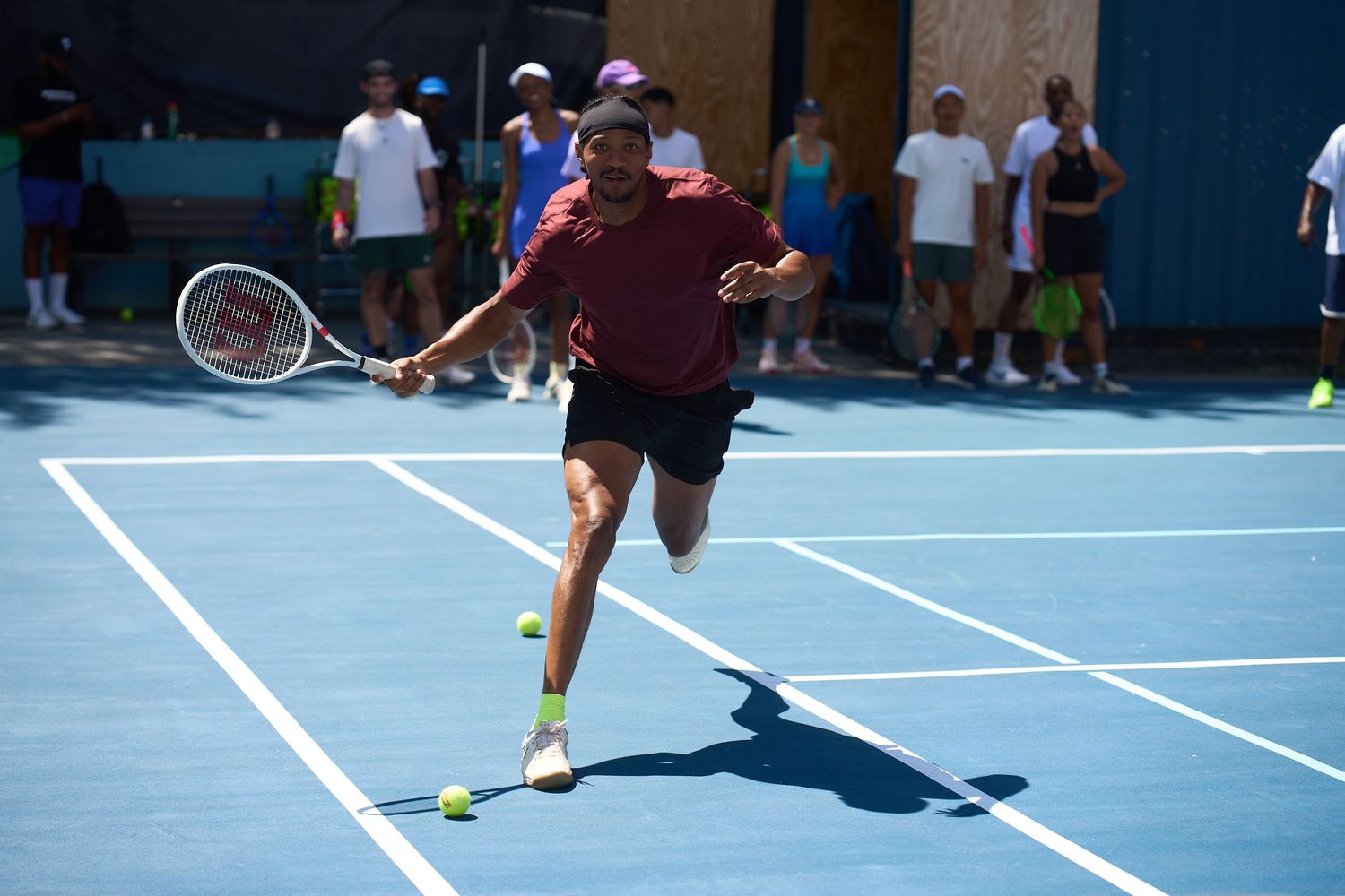 Tennis player stretching to return a shot on a blue outdoor court during practice.