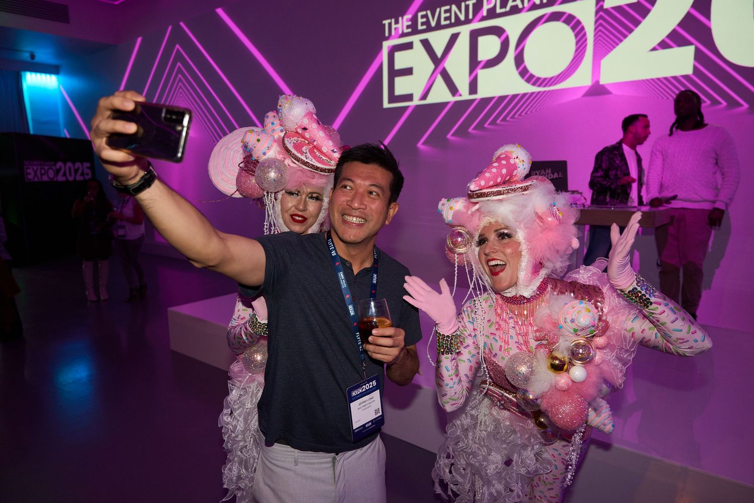 Event attendees celebrate at an expo venue with vibrant purple lighting and energetic party atmosphere.