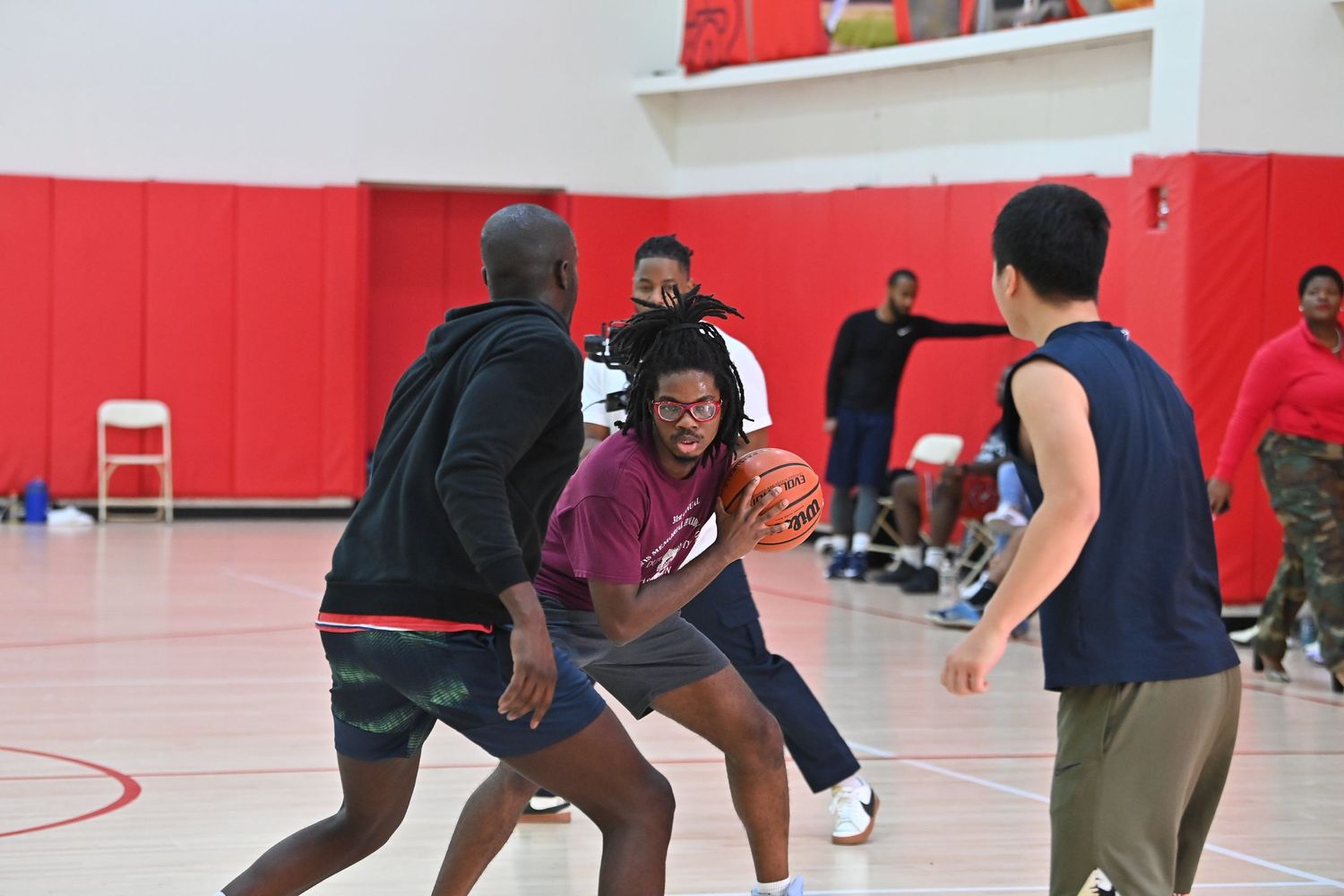 Basketball players compete in a red-walled gymnasium during an intense game or practice session.