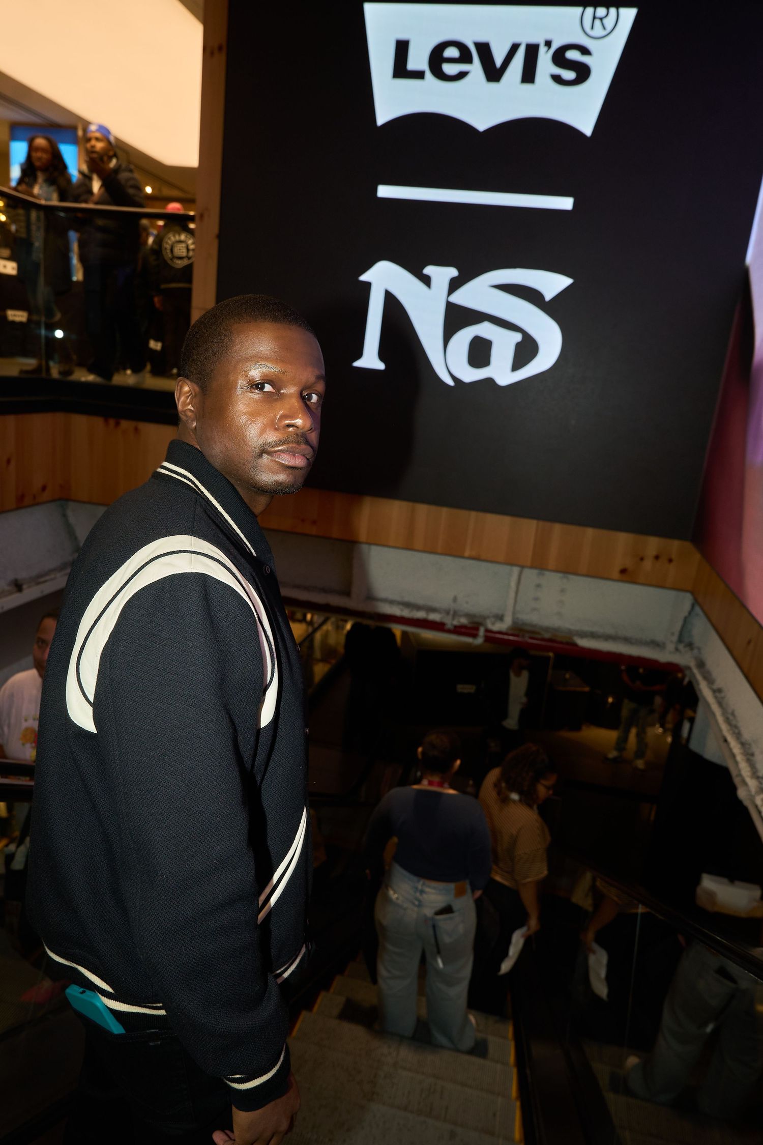 A person in a black varsity jacket with cream stripes poses in front of a Levi's store display.