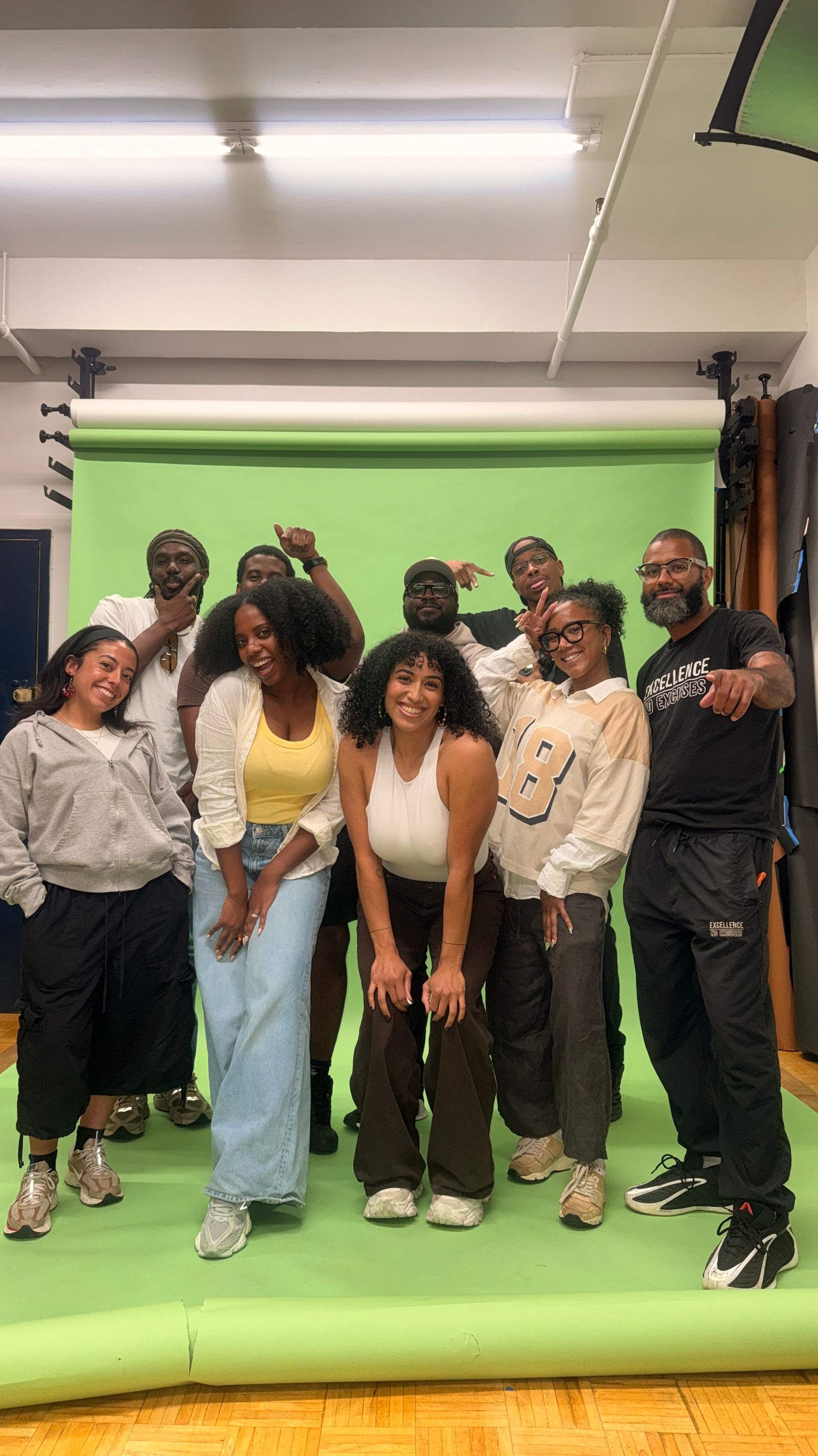 Group of young people posing together in front of a green screen backdrop in a photography studio.