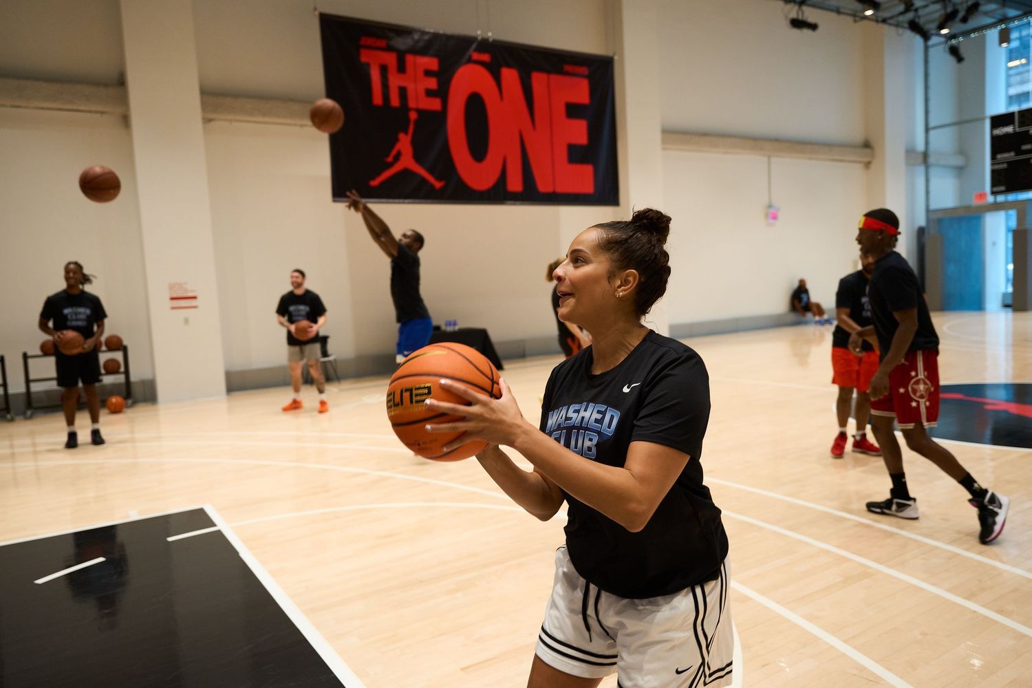 A person performs basketball shooting drills while training in a bright indoor practice facility.