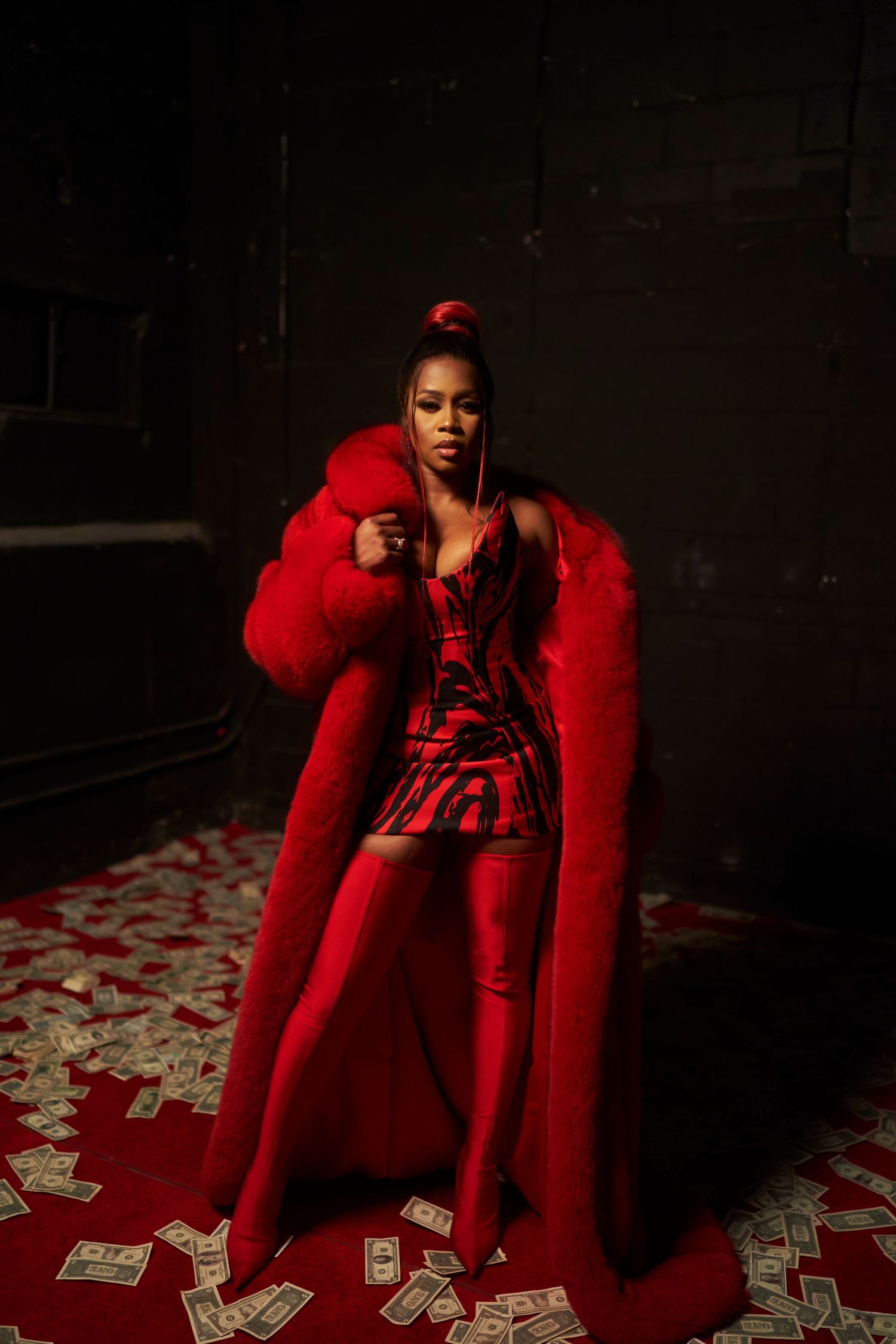 Stylish figure in a bold red outfit and fur coat poses dramatically on floor covered with scattered money.