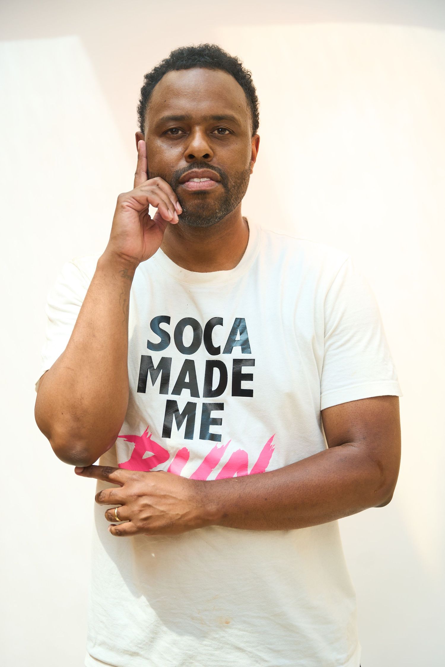 Man in white Soca Made Me Run t-shirt posing thoughtfully with finger raised against light background.