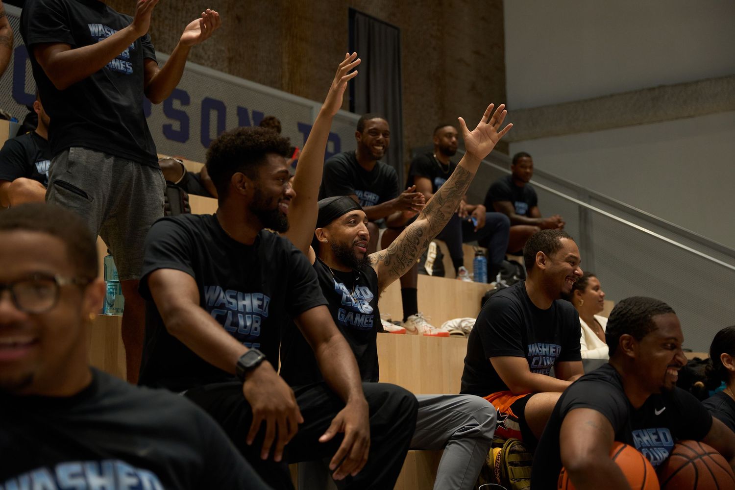 Basketball fans in matching shirts cheer enthusiastically from the bleachers during an indoor game.