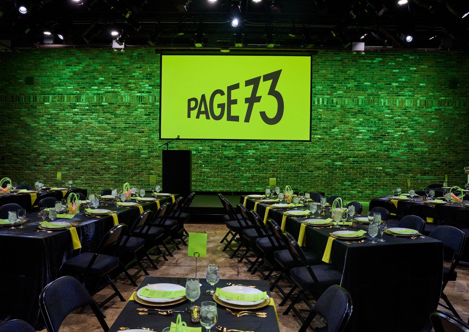 Conference room setup with round tables and glowing green walls illuminated by spotlights for an event.