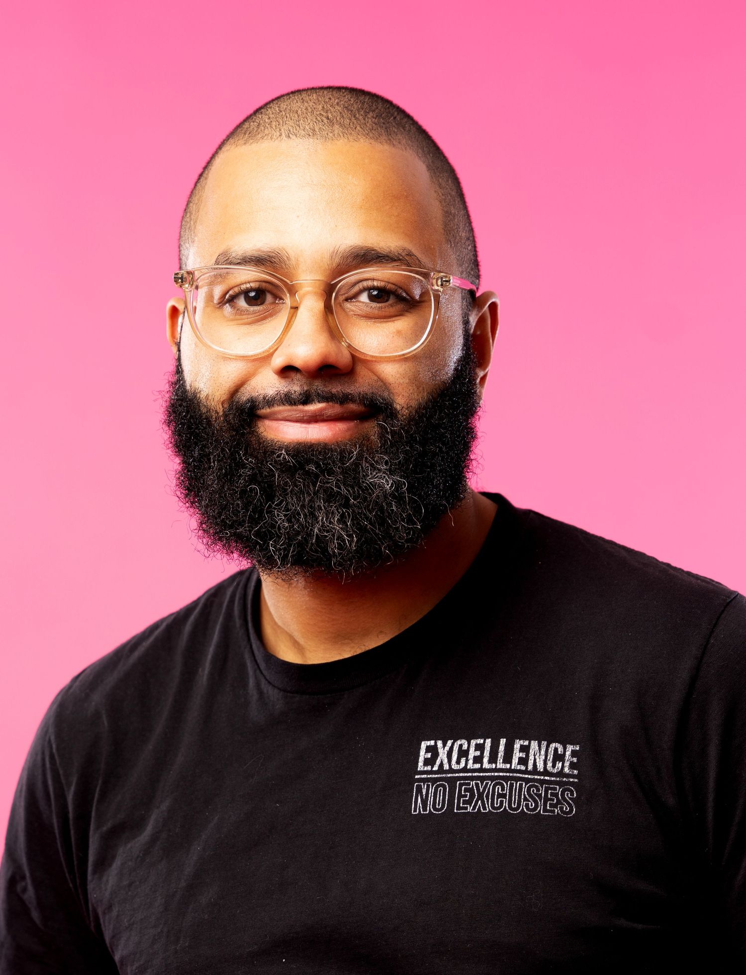 Professional headshot of Daniel J Vasquez wearing glasses and a black t-shirt with 'Excellence No Excuses' text against a pink background.