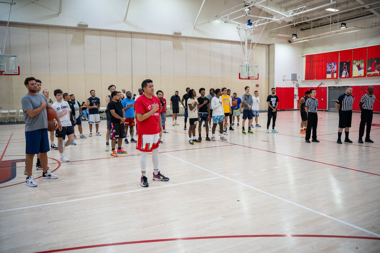 Students participate in physical education activities in a large indoor gymnasium with red and white walls.