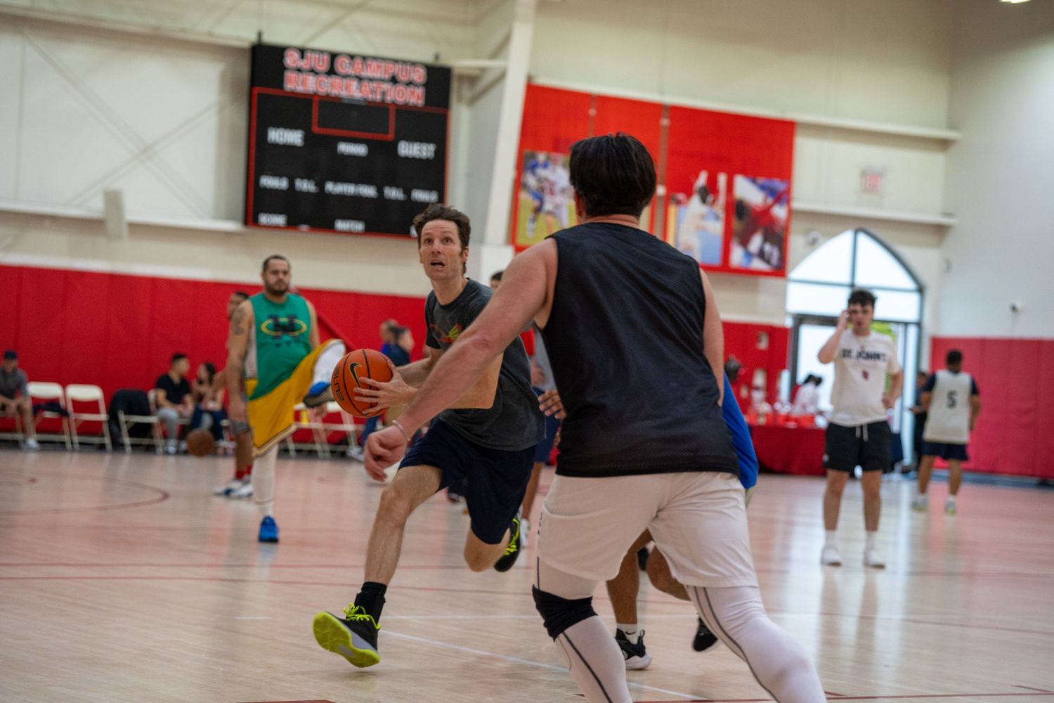 Basketball players compete in an indoor game on a red-floored gymnasium court during a recreational match.