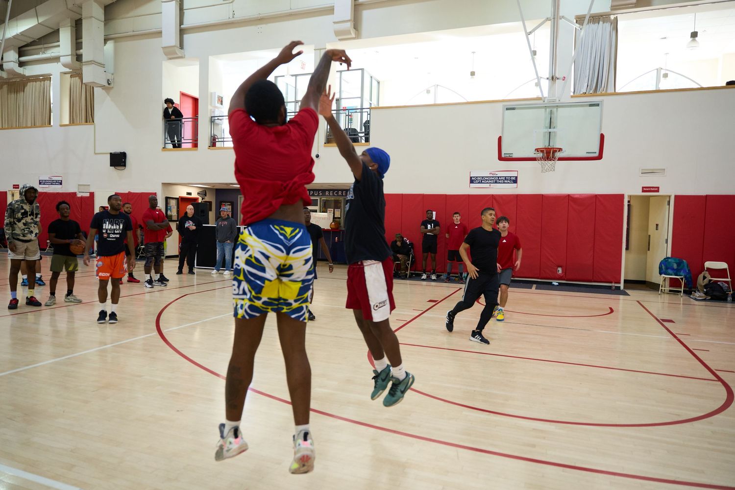 Basketball players practicing drills in a spacious indoor gymnasium with red and white walls.