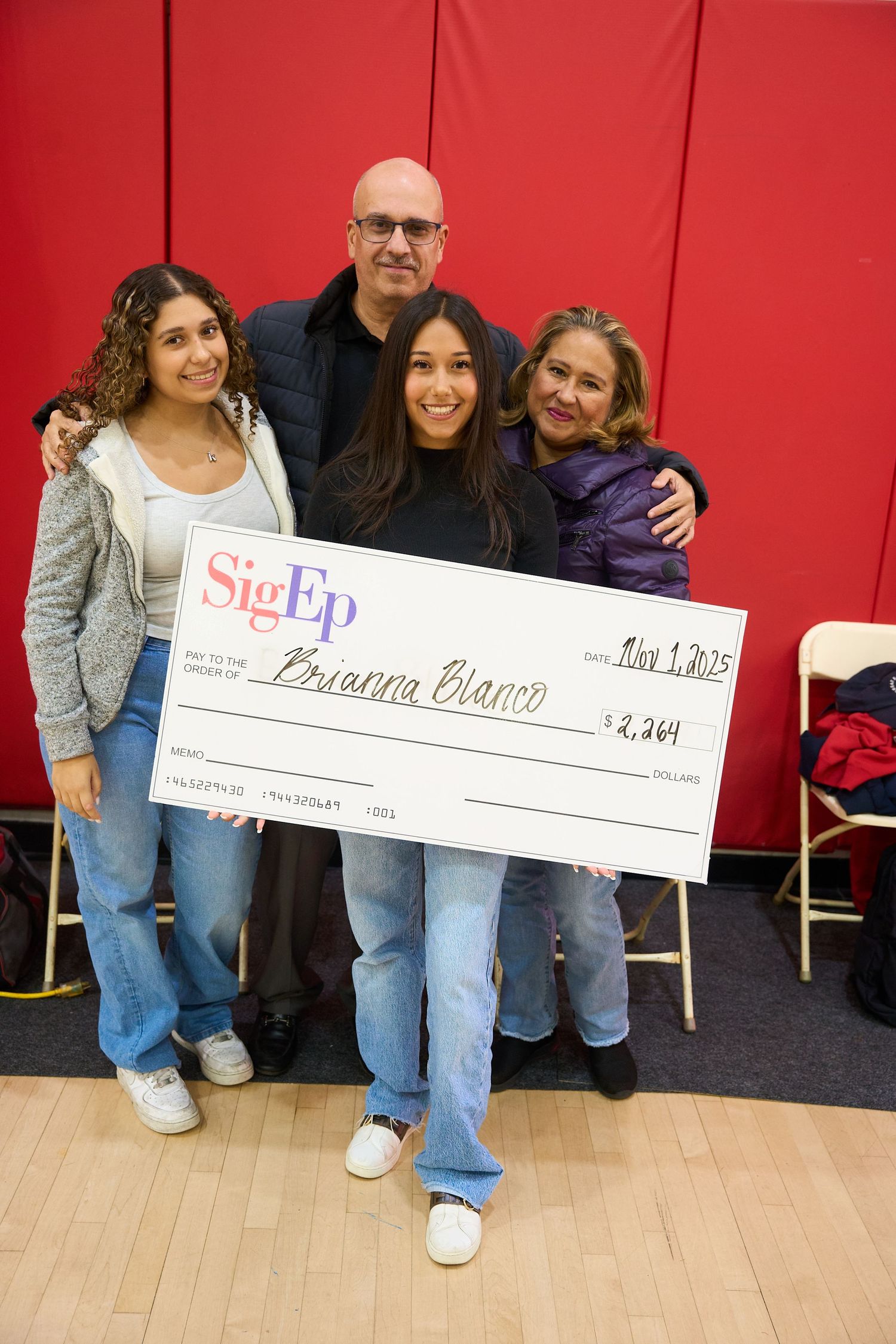 Group posing with large ceremonial checks in a gymnasium setting.