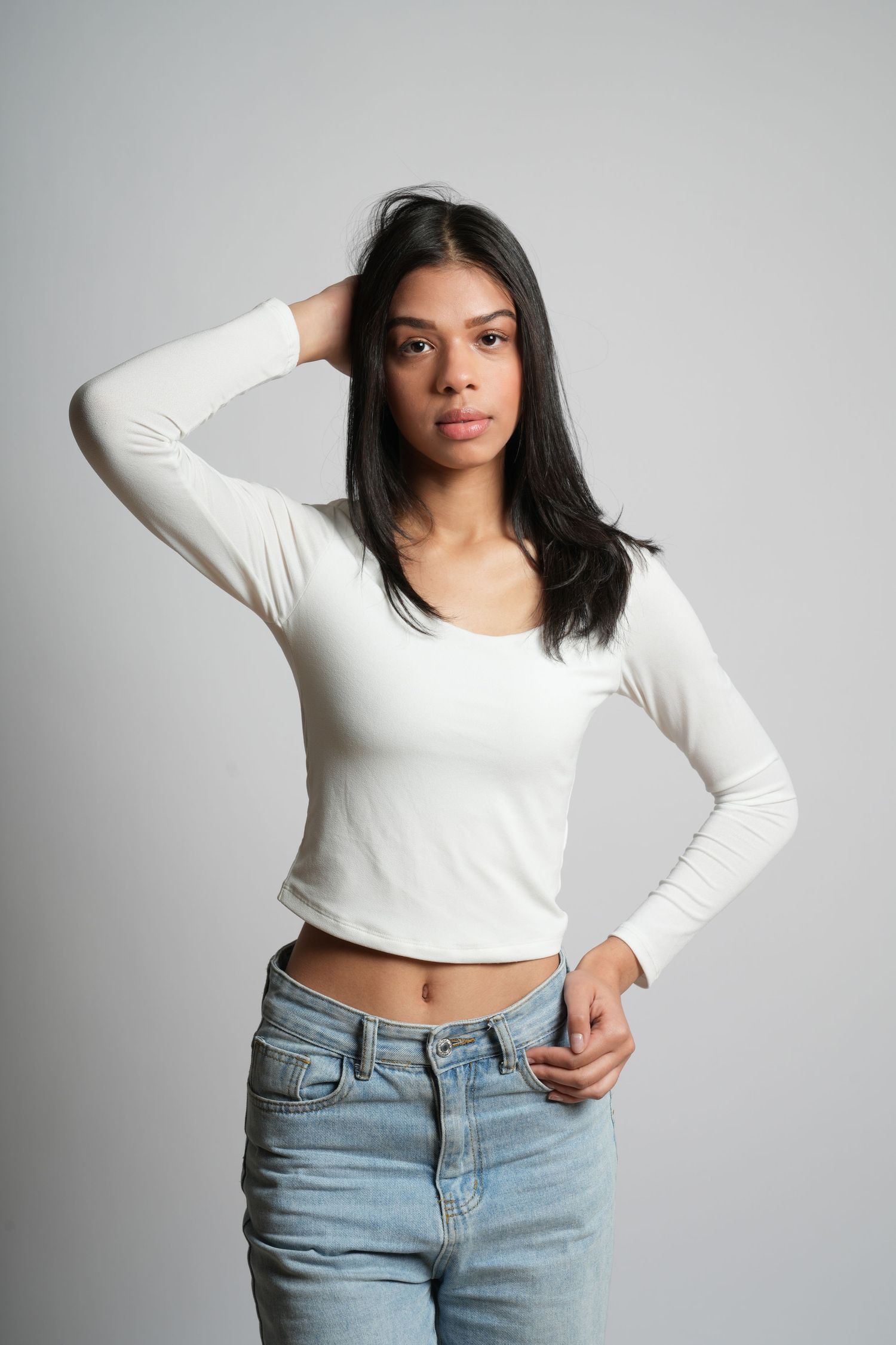 A model in a white long-sleeve crop top and light blue jeans poses against a gray background in a series of photos.