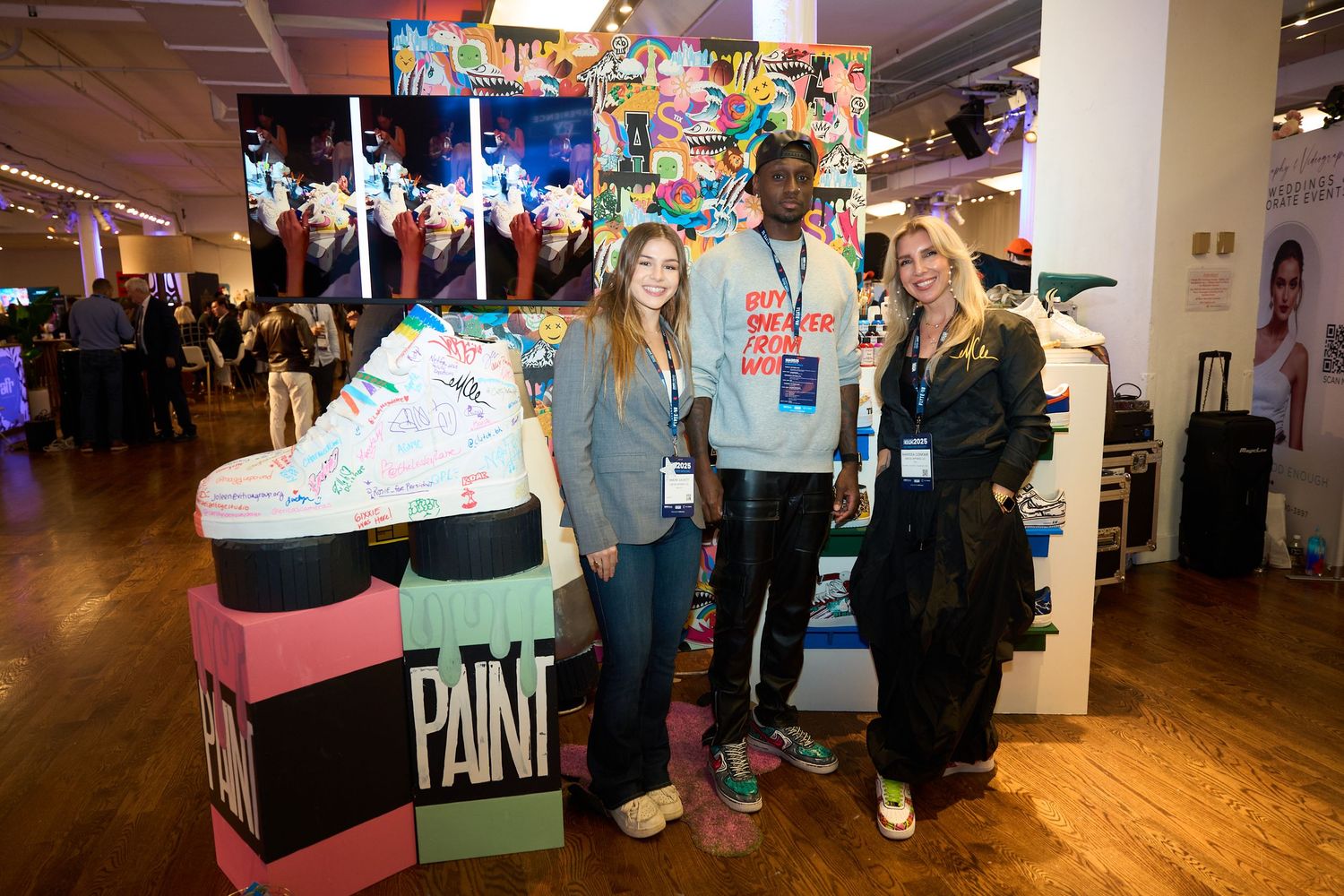 People gather at an indoor event space with colorful decorations and signage visible in multiple connected rooms.