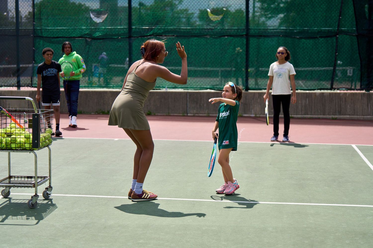 Tennis players practice drills and techniques on outdoor court during daytime lesson.