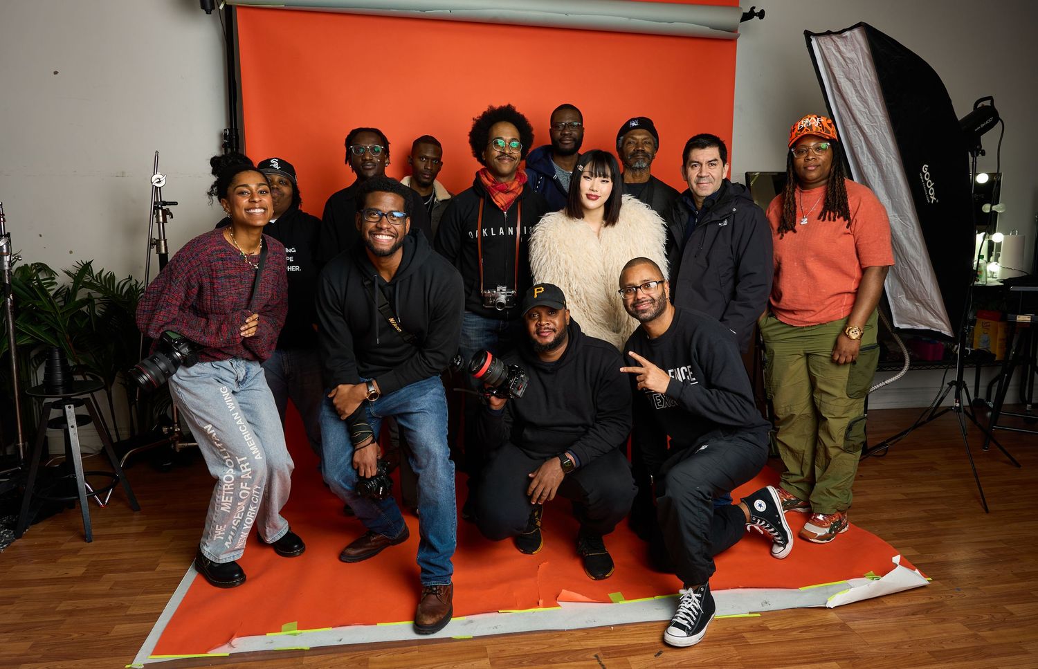 Group photo of creative team members posing together in photography studio with orange backdrop and lighting equipment.