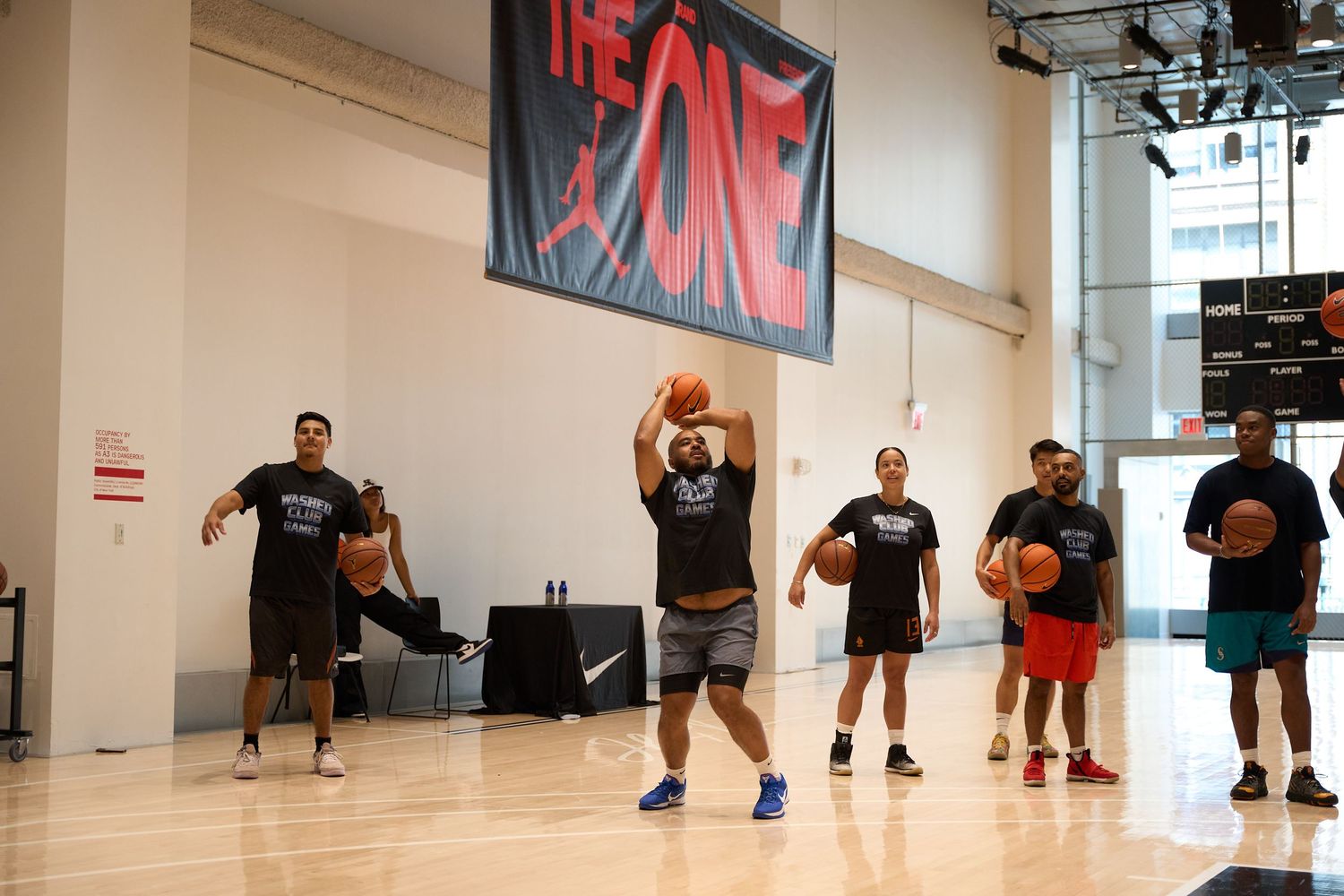 Panoramic view of a basketball training class with players practicing dribbling drills in a bright indoor gymnasium.