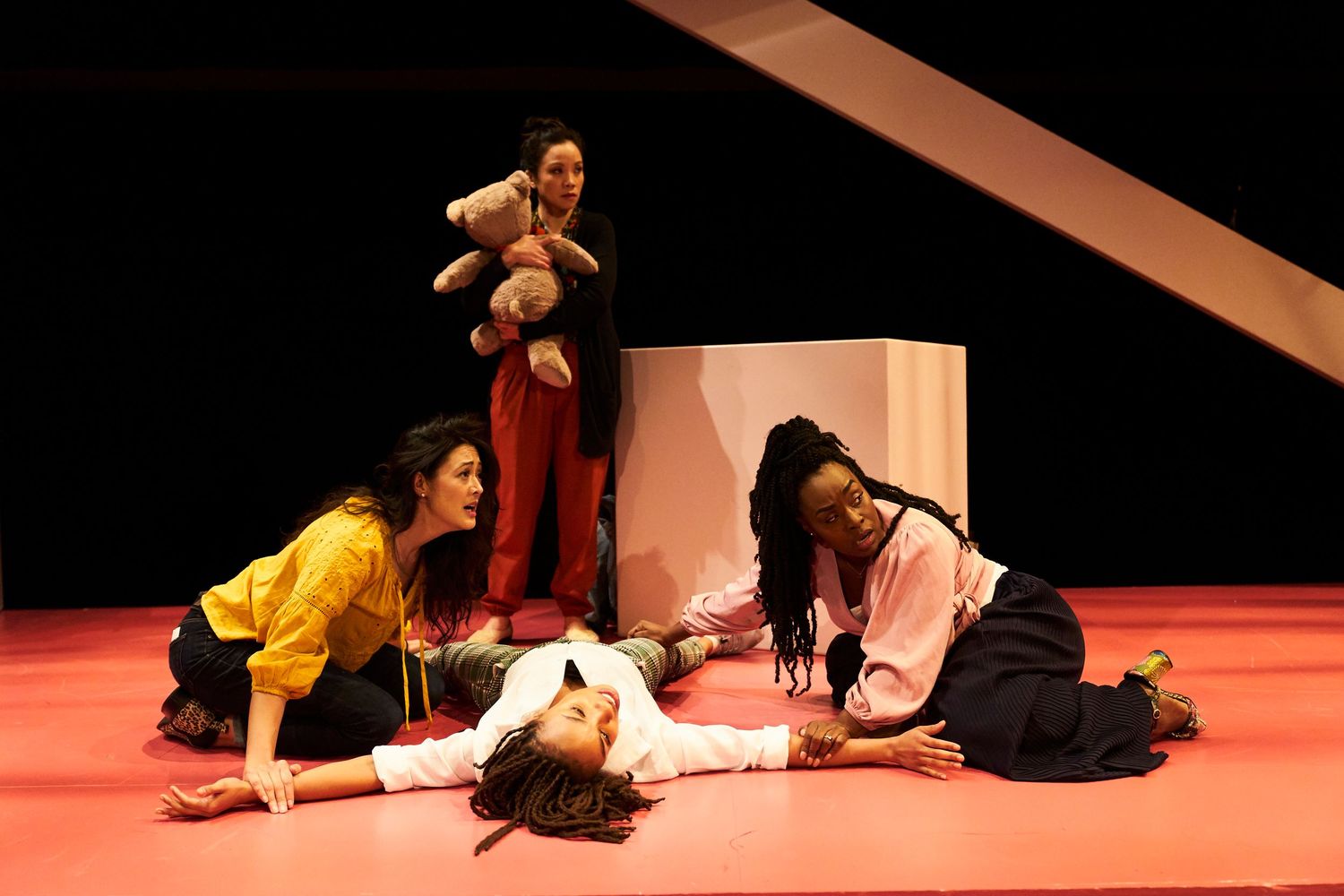 Theatrical performers engage in dramatic poses on a red stage with a soft toy prop visible during a play performance.