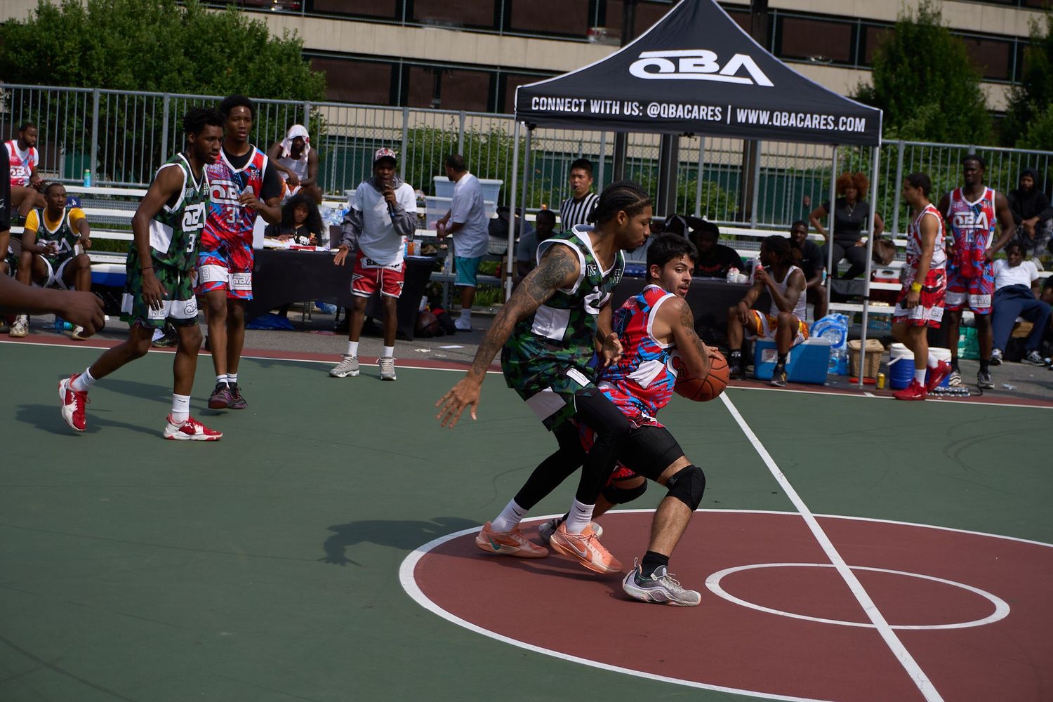 Basketball players compete in an outdoor street basketball game on a green court during a tournament.