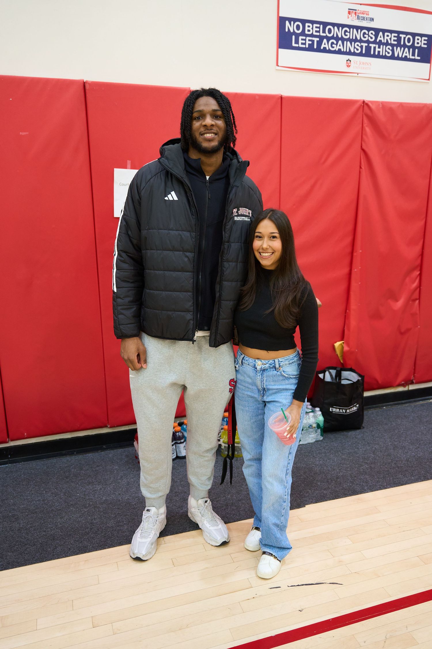 People posing together in a gym with red walls and basketball court markings.
