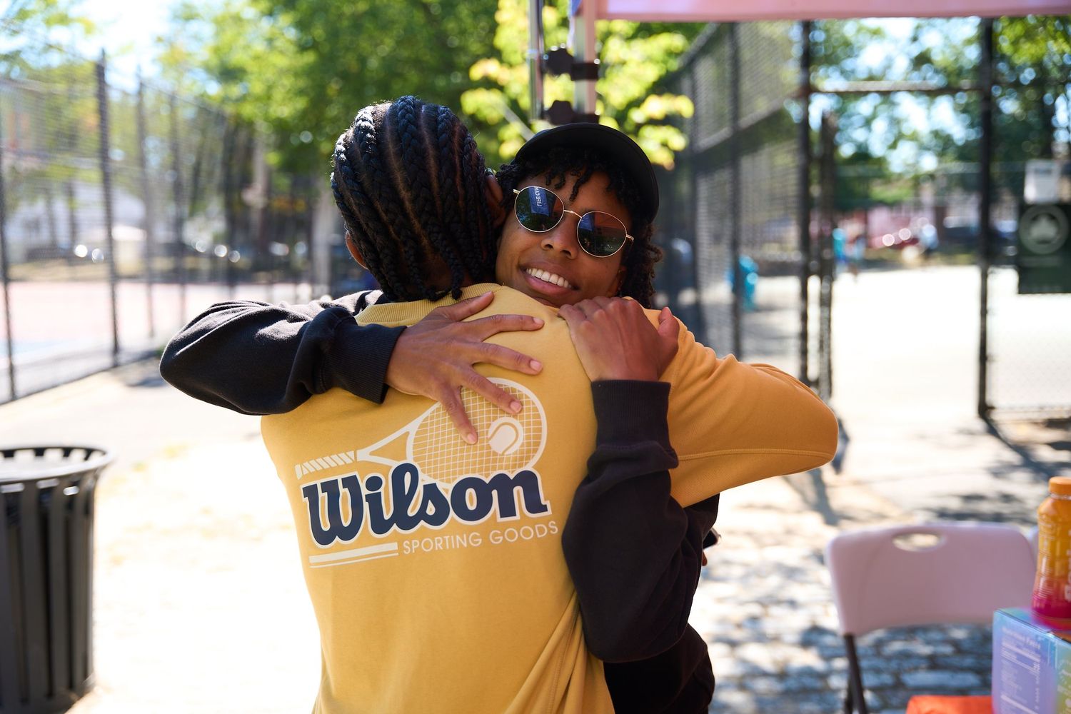 People embracing and celebrating at an outdoor tennis court on a sunny day.
