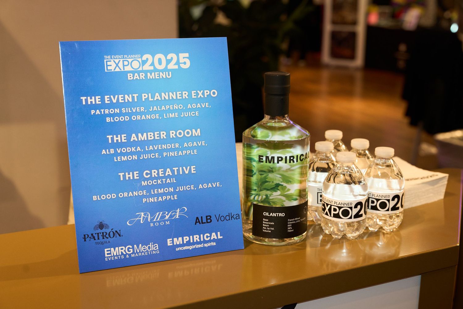 Event planning expo signage and materials displayed on a wooden table with blue banners and glass decor items.