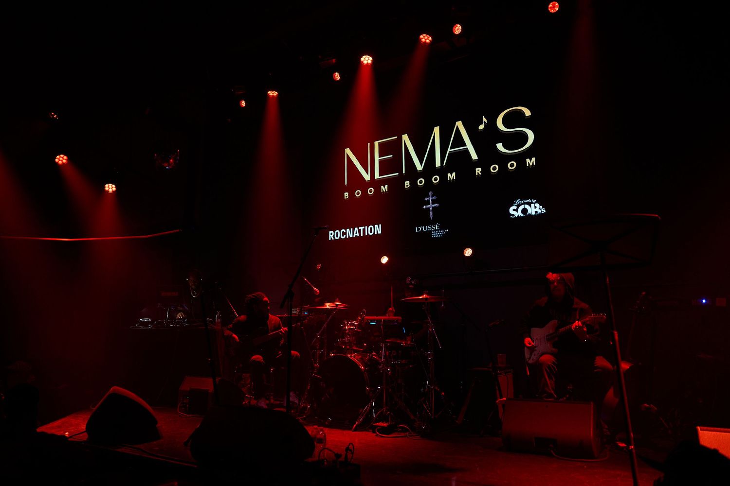 Red-tinted nightclub interior with glowing lights and dark silhouettes creating a moody atmospheric ambiance.