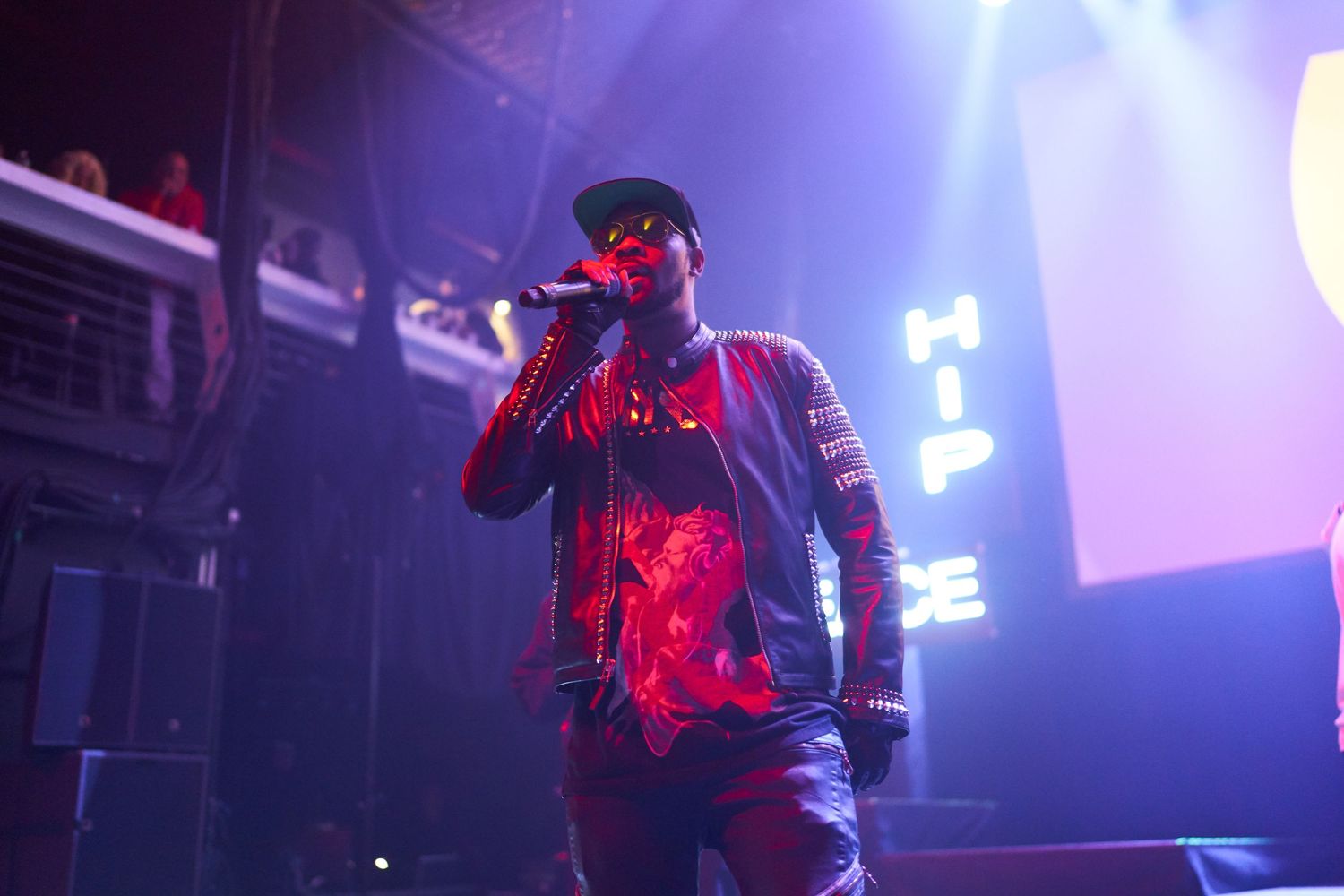 Performer silhouetted in red and blue stage lighting during a concert with illuminated signage in background.