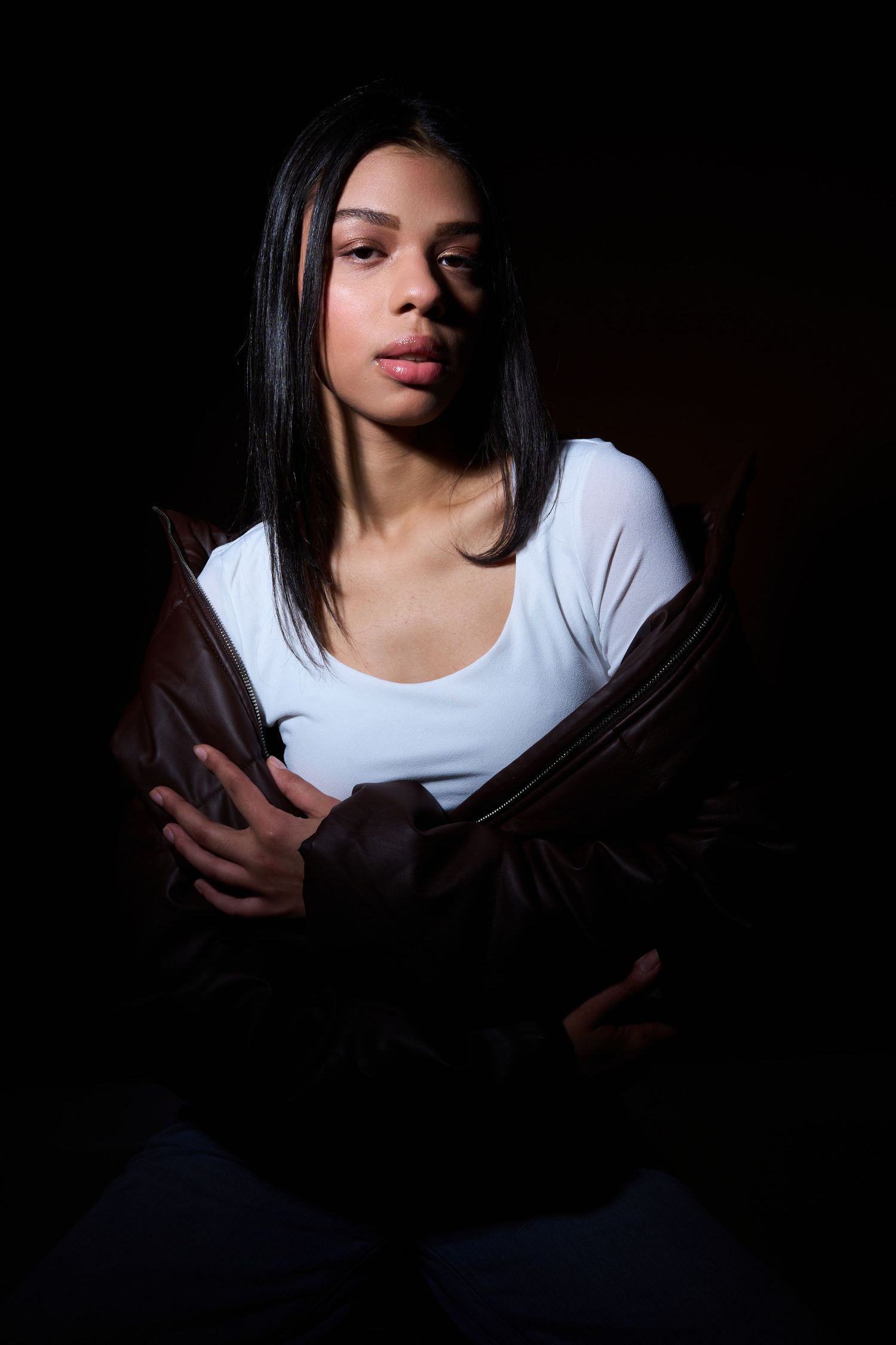 A figure in a white top emerges from dark shadows in a dramatic low-key portrait series.