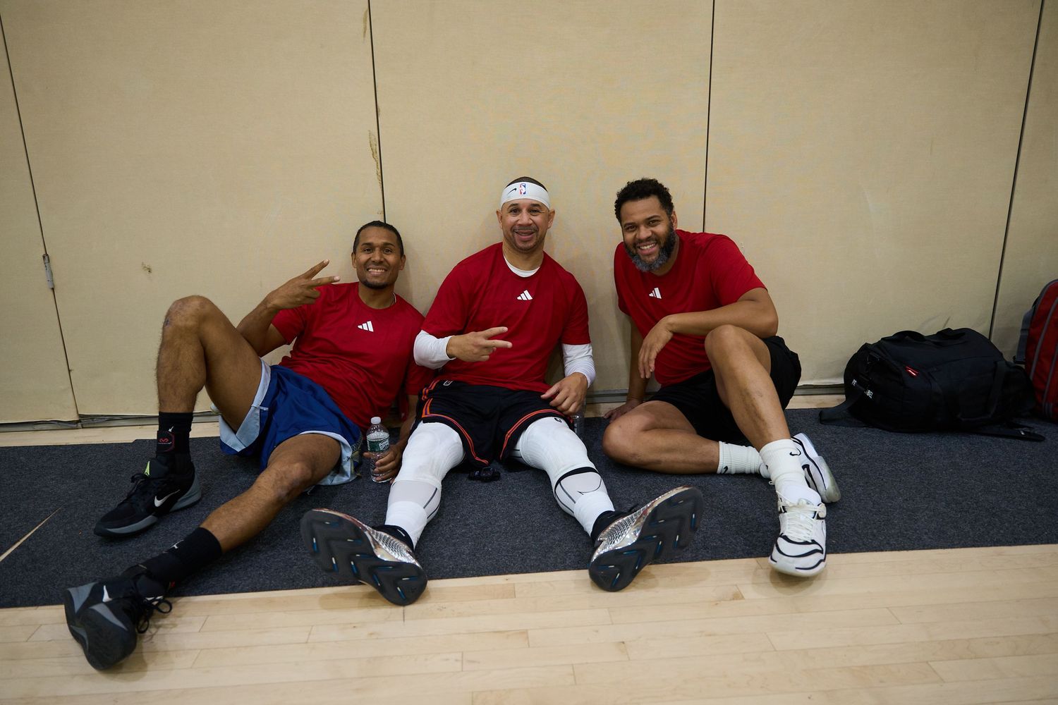 Three athletes resting on the floor against a wall in matching uniforms.