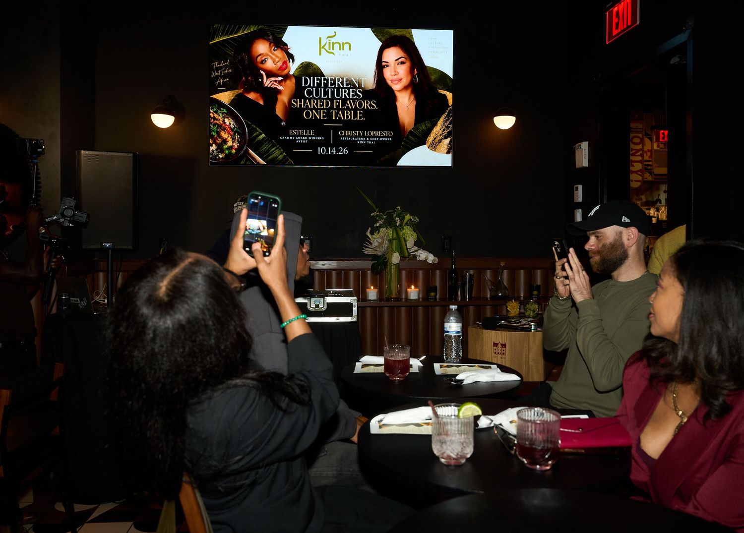 Guests at a dimly lit restaurant table photograph a screen reading 