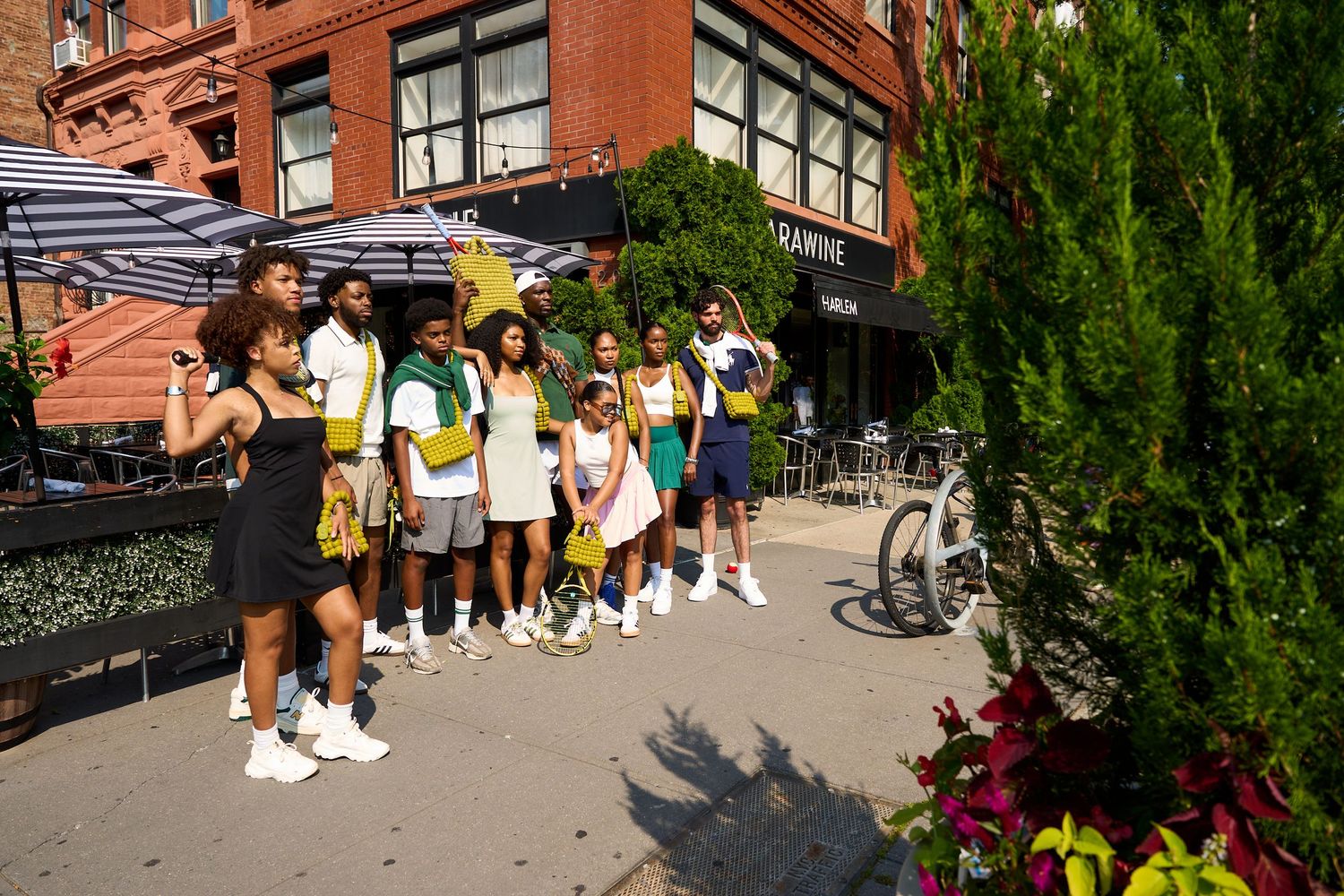 Crowds gather behind barriers near brick buildings and greenery during an outdoor event.