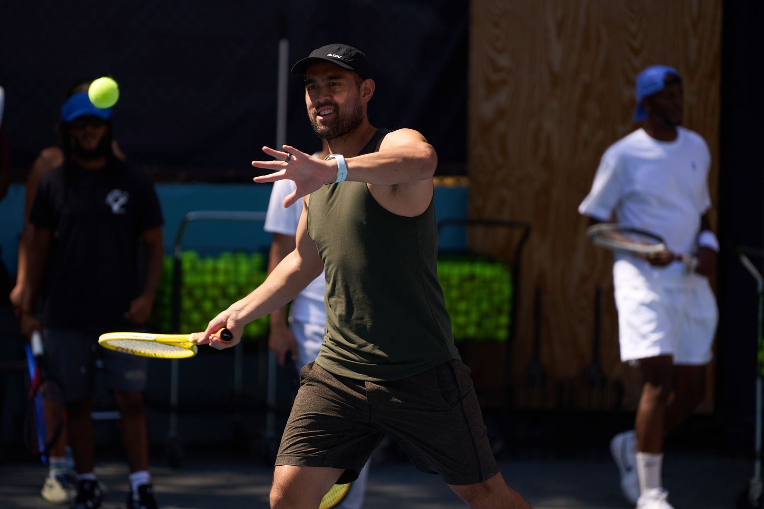 Tennis players practicing serves and volleys on a blue outdoor court during a sunny day.
