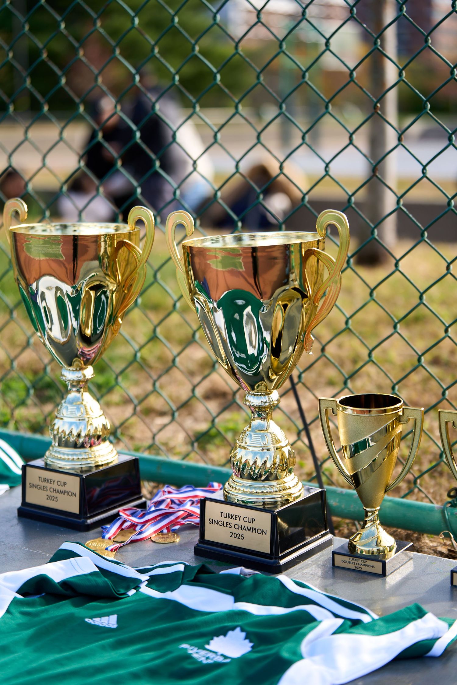 Gold and silver sports trophies and medals displayed on green jerseys at an outdoor sporting event awards ceremony.