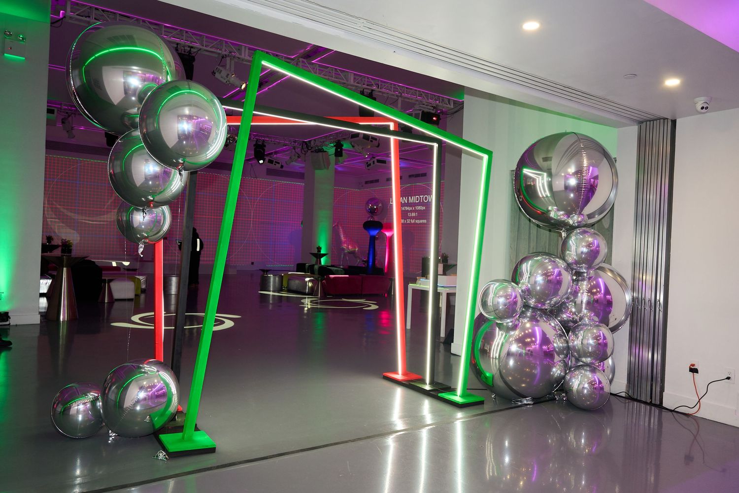 Modern event space with silver balloon decorations, green neon lighting and geometric frame structures.