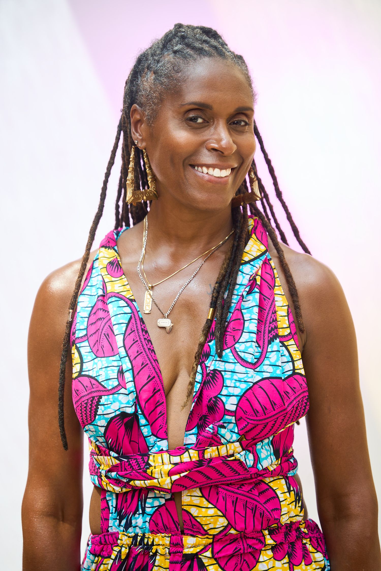 Smiling woman with long braids wearing a colorful tropical print halter dress and layered necklaces.