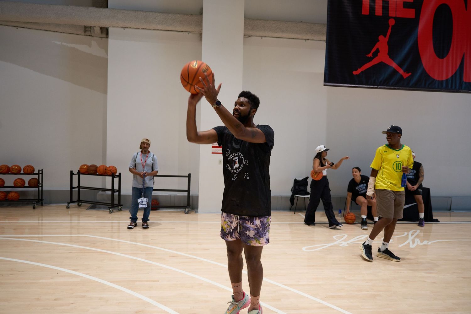 Basketball player takes a shot in an indoor gym with others practicing in the background.