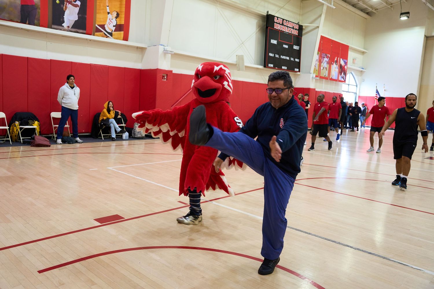 A mascot in red costume interacts with someone in blue during a gym event.