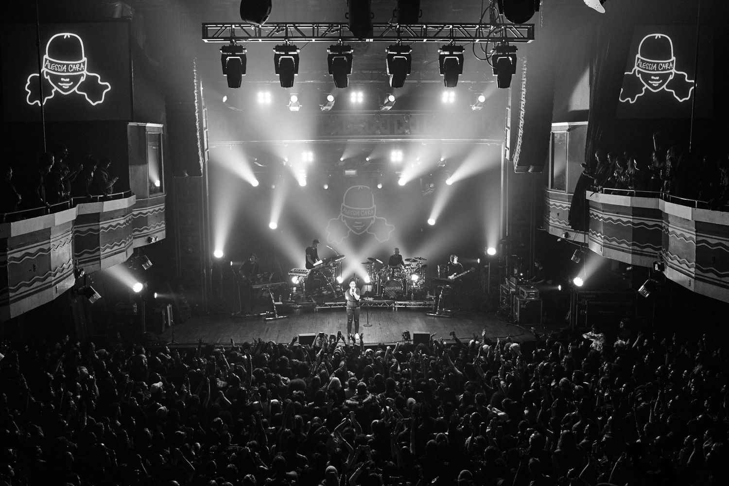 Black and white concert photo showing a performer on stage with dramatic lighting and a large crowd during a live performance.