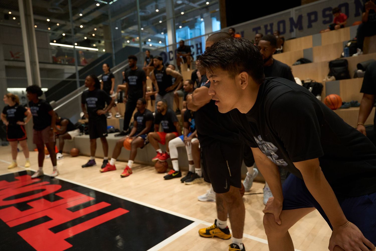 Athletes prepare before competing at an indoor basketball court with red floor markings.