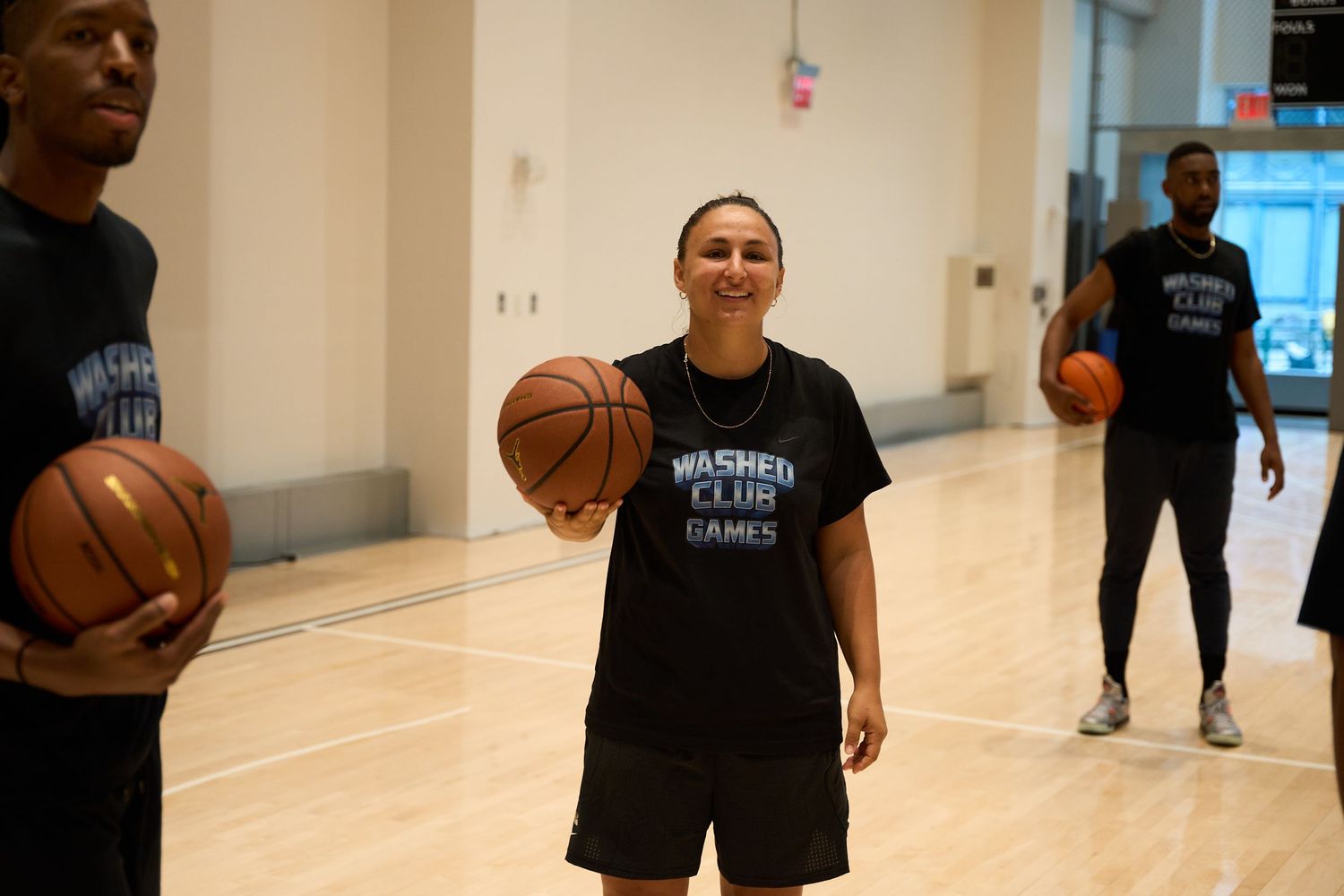 A person in a black shirt plays basketball indoors, demonstrating dribbling skills on a court.