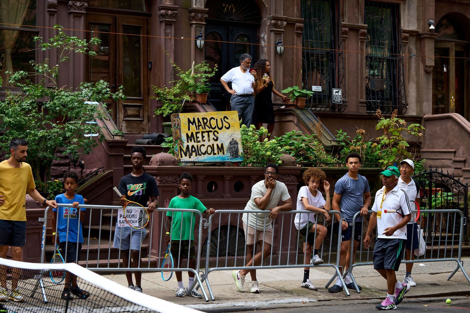 People enjoying outdoor activities at a bustling urban park with brownstone buildings in the background.