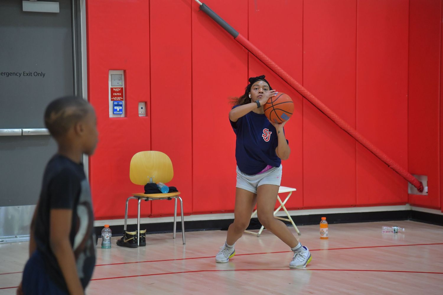 A red-walled gymnasium with players practicing basketball drills and exercises on the hardwood court.
