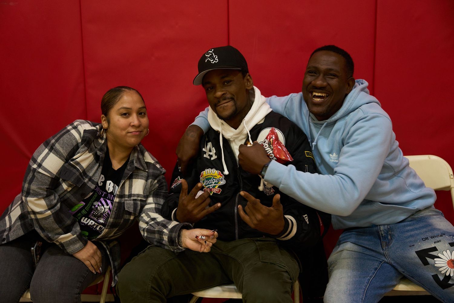 Group of students laughing and socializing together in a casual indoor setting with red wall background.