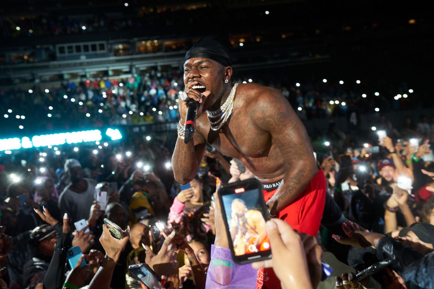 Performer singing on stage with crowd and bright spotlights during energetic concert performance.
