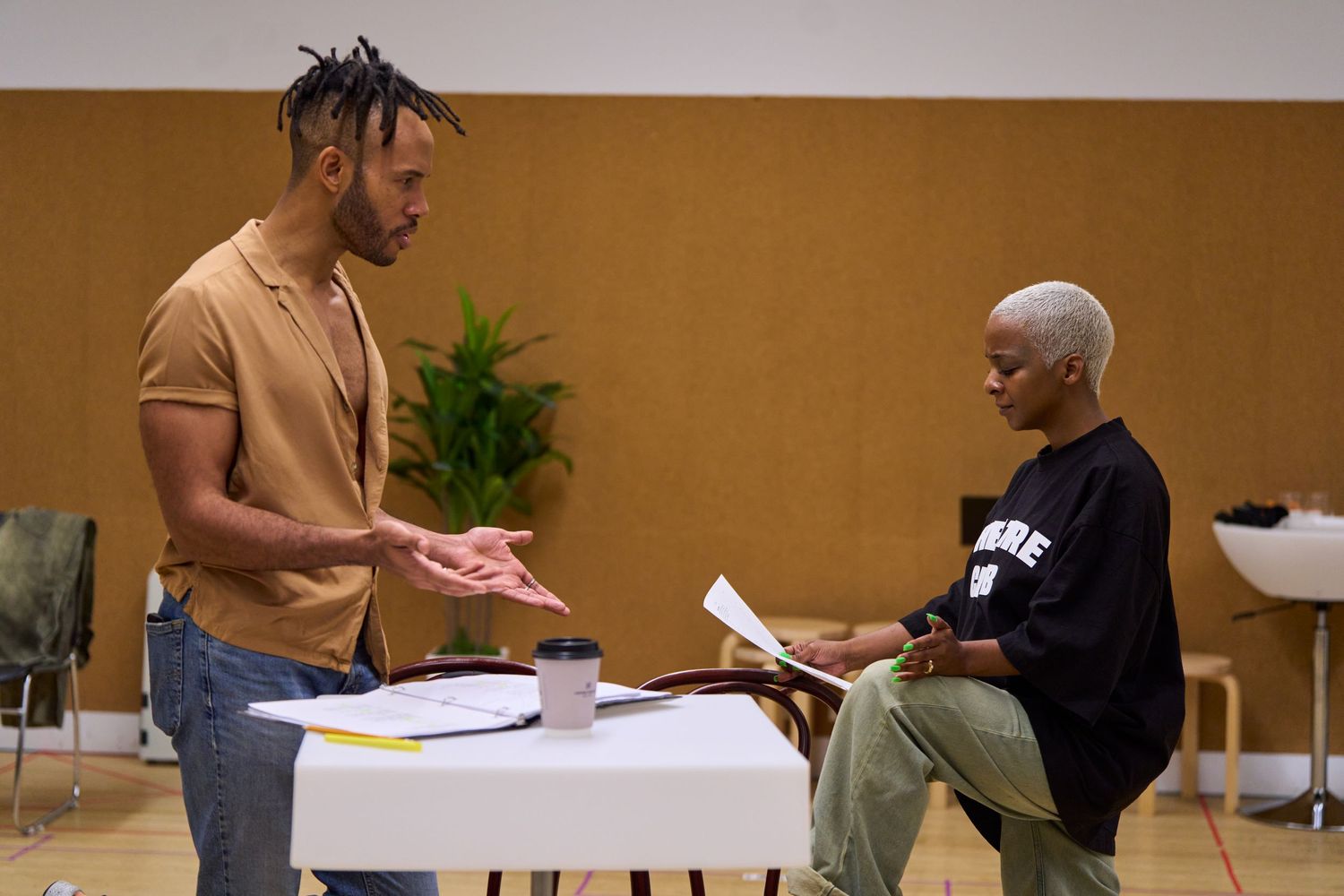 Two people interact while standing at a table with papers in what appears to be a meeting room.