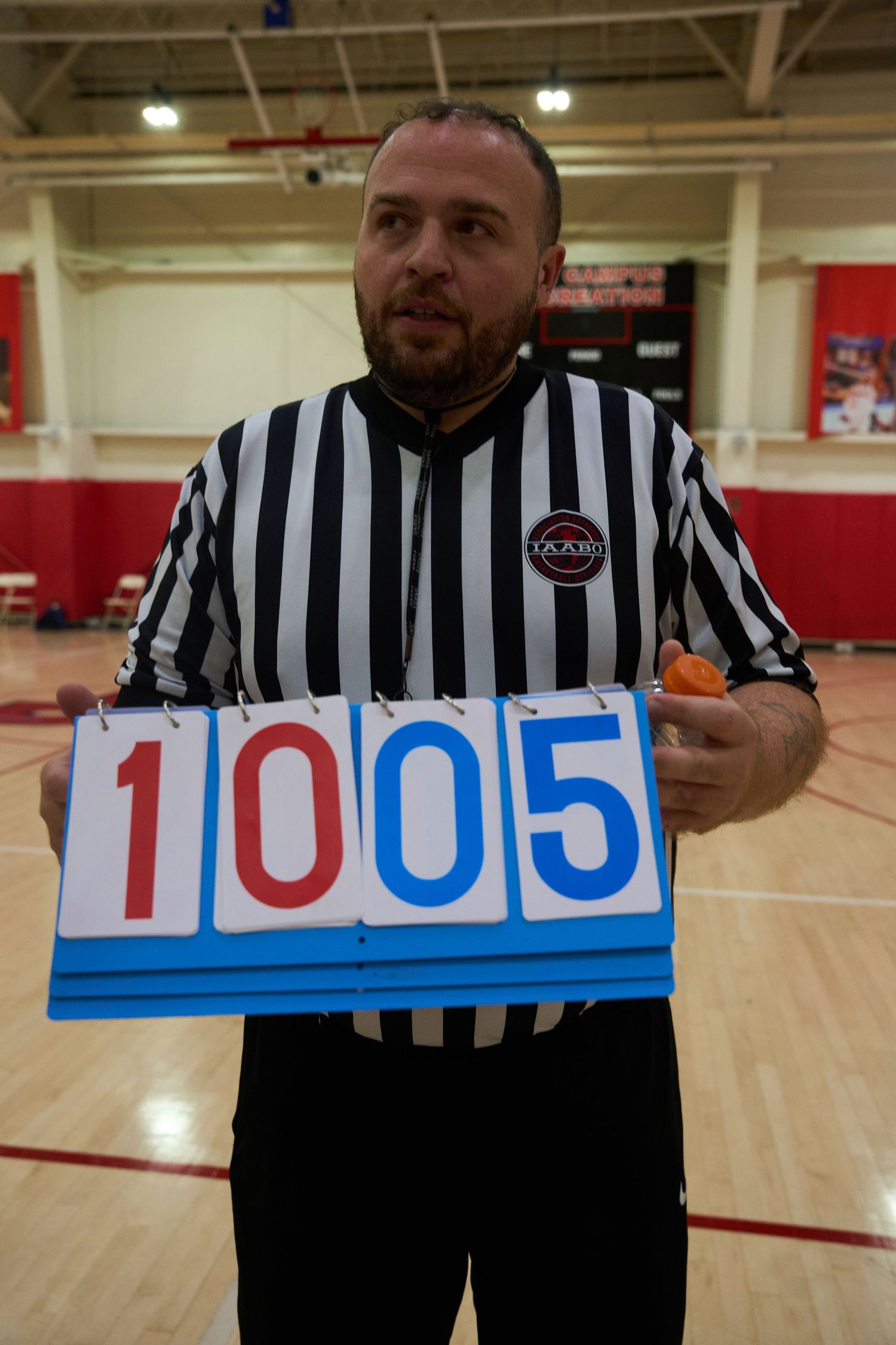 Referee displaying score cards showing numbers in blue and white against a gymnasium background.