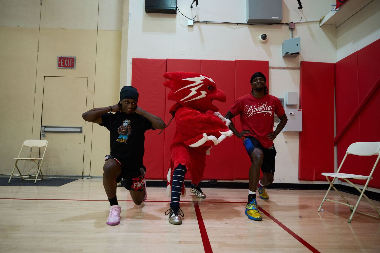 Athletes practicing breakdancing moves on a red gymnasium floor during a dance session.