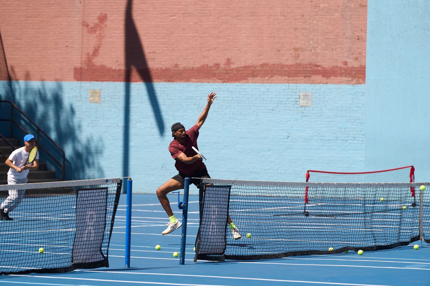 Athletes play pickleball on a vibrant blue court against a terracotta-colored wall backdrop.
