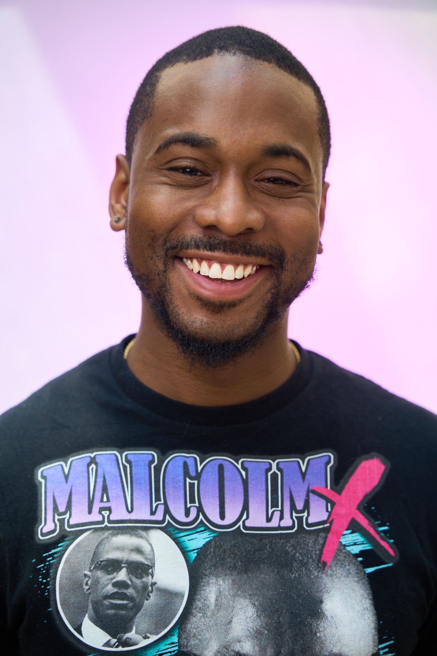 Smiling young man wearing a Malcolm X graphic t-shirt against a purple background.