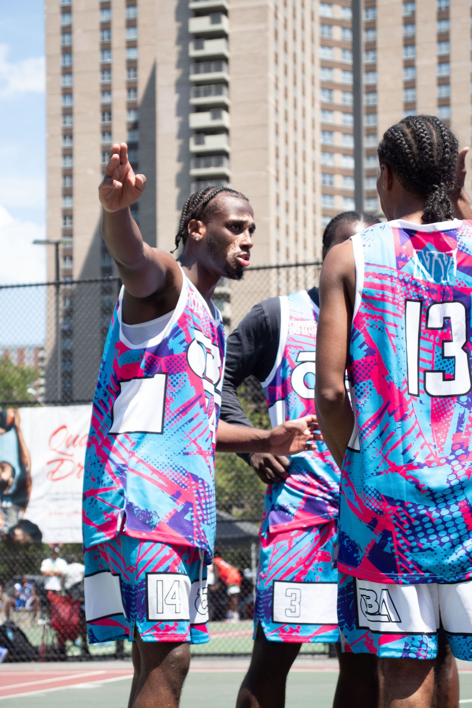 Basketball players wearing bright pink and blue patterned jerseys during an outdoor street basketball game.
